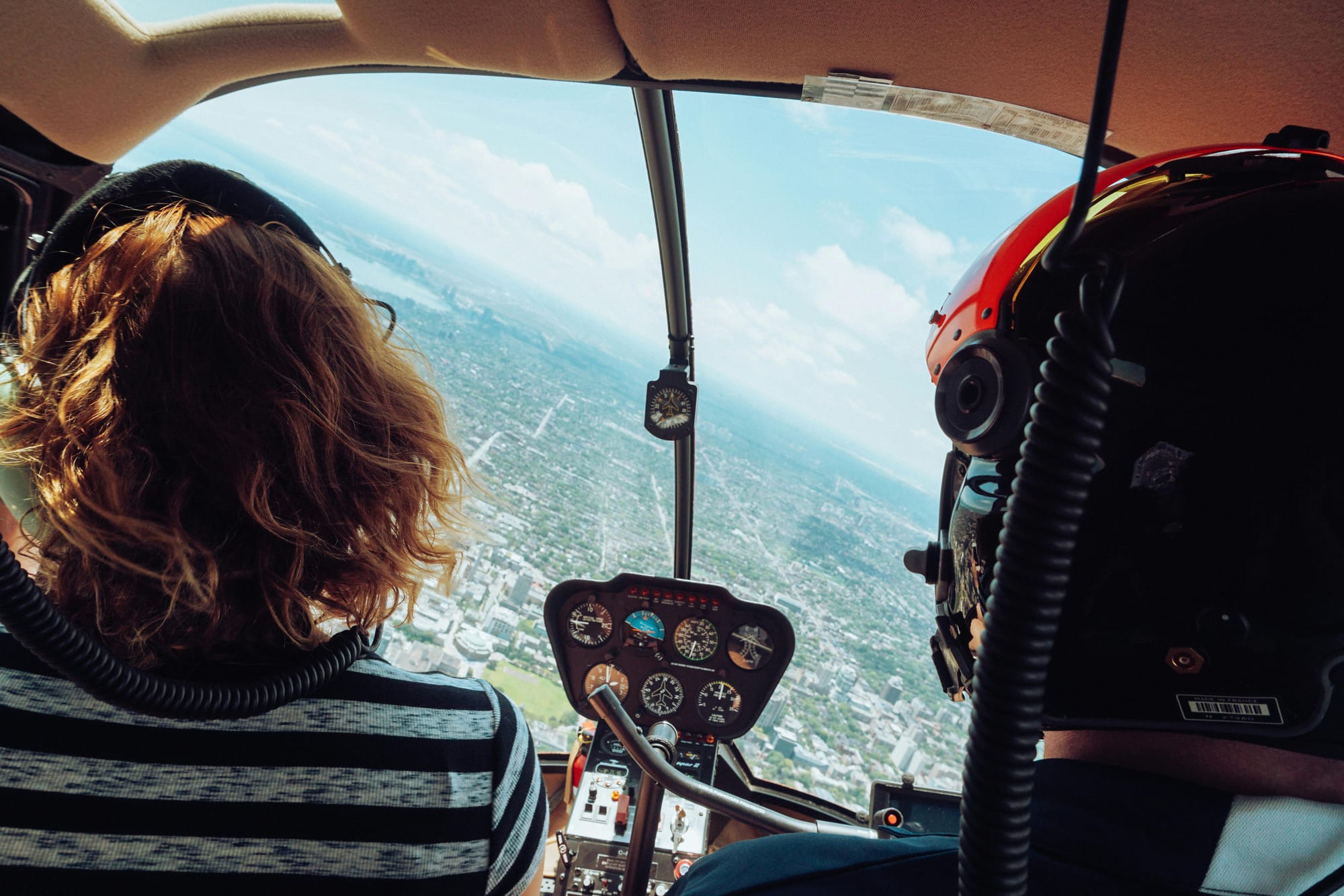 View out of the windscreen of an R44 helicopter. Showing a passenger and pilot. The pilot is wearing a helmet.